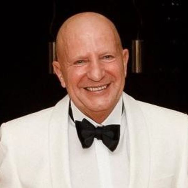 Smiling bald man in a white tuxedo with a black bow tie.