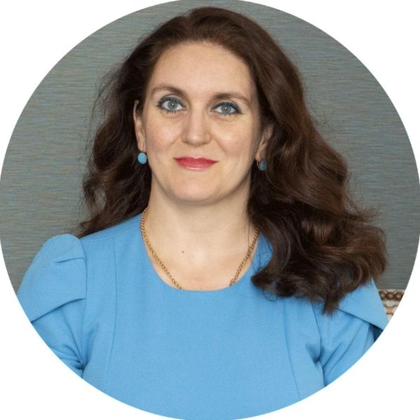 Woman with brown hair wearing blue dress and matching earrings.