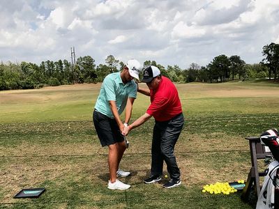 Golf instructor teaching a student on a driving range with yellow balls.
