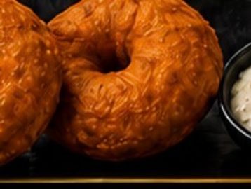 Two glazed donuts and a small bowl of cream.