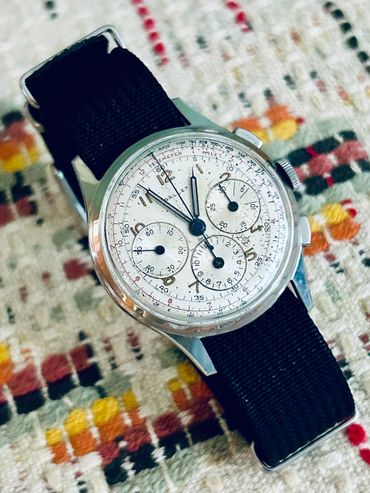 Vintage wristwatch with black strap on a patterned fabric.