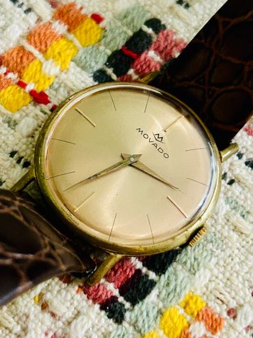 Close-up of a vintage Movado wristwatch with a leather strap on a textured fabric.