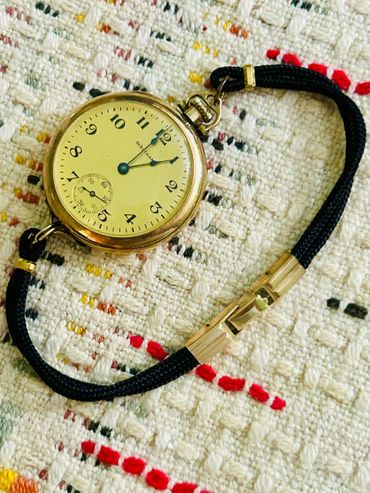 Vintage Waltham pocket watch with black cord on textured fabric.