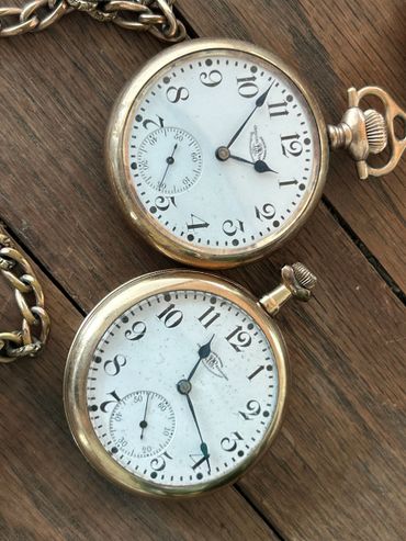 Two vintage gold pocket watches on a wooden surface.