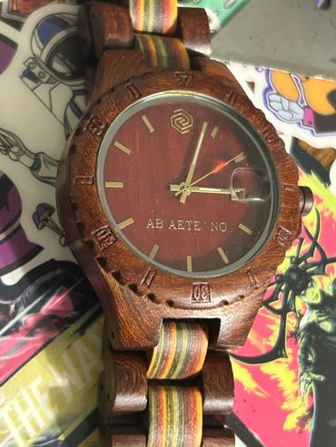 Wooden wristwatch with a multicolored band and gold accents.