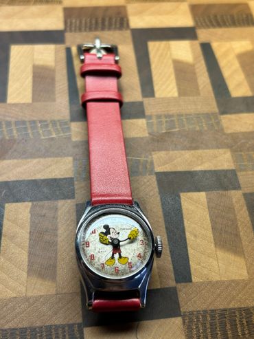 Vintage Mickey Mouse watch with red leather strap on patterned surface.