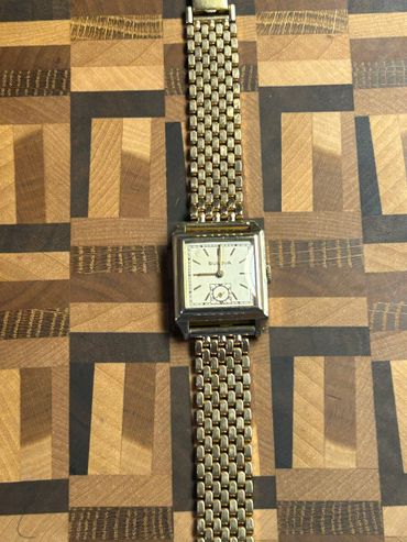 Vintage Bulova wristwatch with gold-tone bracelet on a patterned wooden surface.