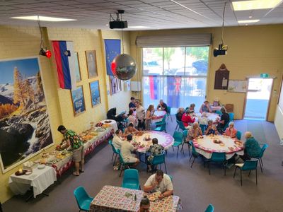 Community gathering with people dining at round tables in a decorated hall.