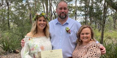 Three people smiling outdoors, holding a certificate, celebrating a special moment.