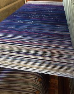 Looking at the back of a loom at the warp in white, blue, purple, and sparkle threads
