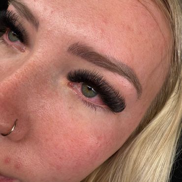 Close-up of a woman's eye with long false eyelashes and a nose ring.