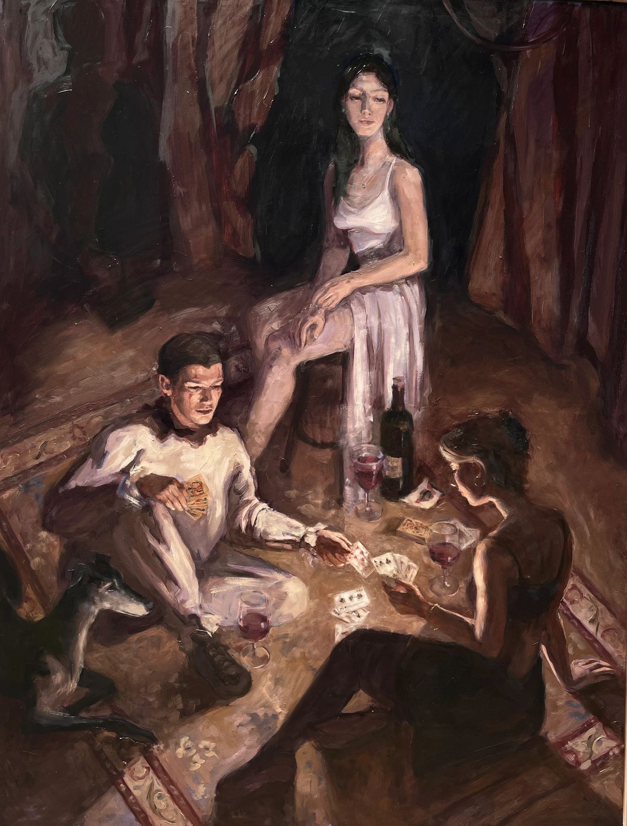 Three people and a dog playing cards with wine in a dimly lit room.