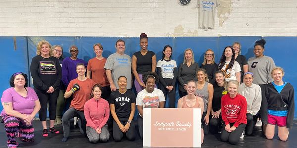 Group of diverse women posing in a gym with a Ladysafe Society sign.