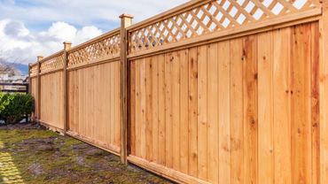 A wooden fence with lattice top panels in a backyard.