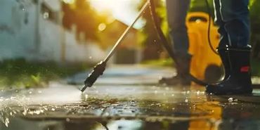Person pressure washing a wet pavement on a sunny day.