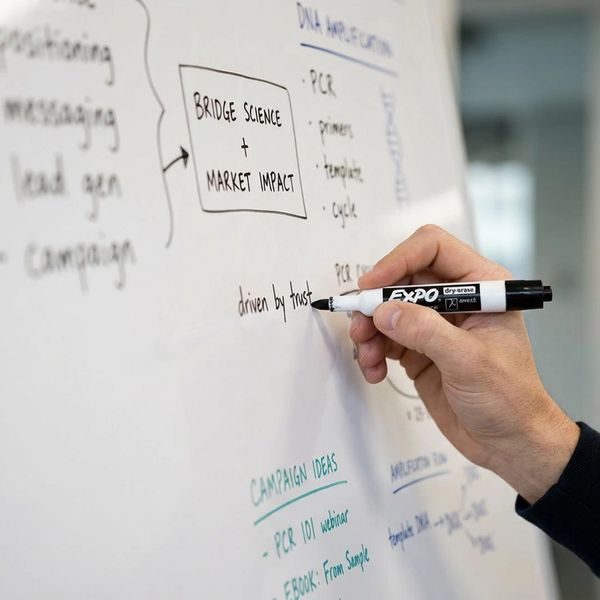 A hand writing on a whiteboard with a black Expo marker.