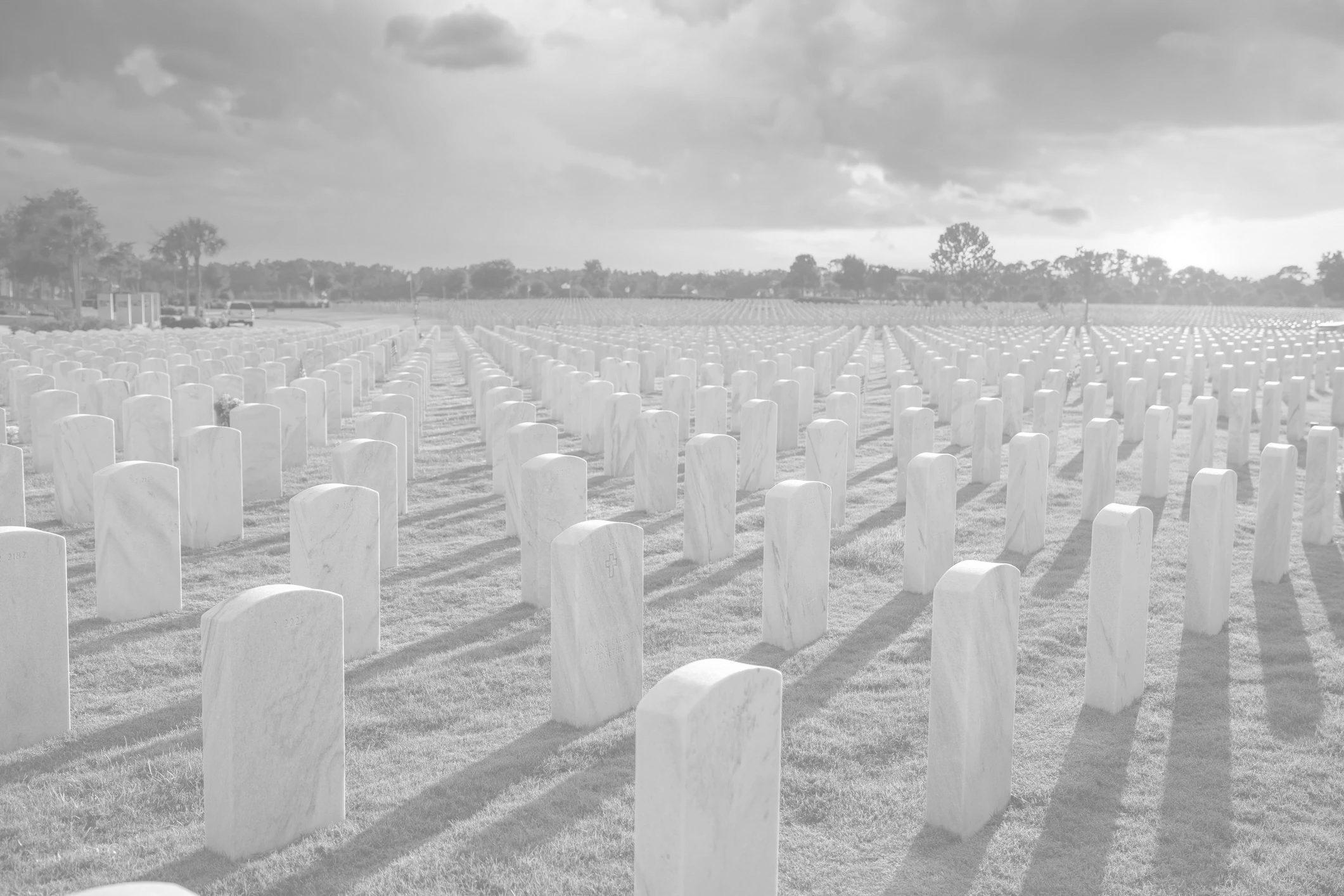 Rows of white gravestones in a cemetery at sunset.