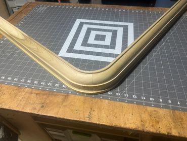 Custom curved wood molding with a rounded corner, resting on a workshop measuring mat.