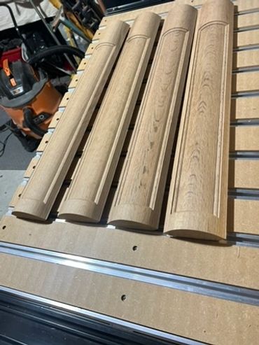 Four shaped wood components with routed details arranged on a CNC machine bed.