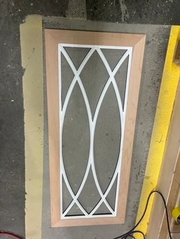 Decorative white cabinet-door mullion with flowing curves and diamond shapes inside a wood frame.