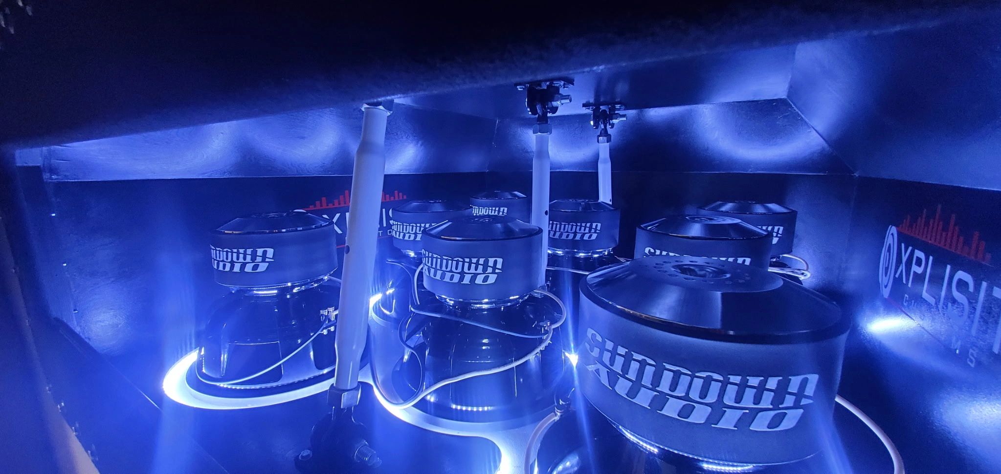 Illuminated Sundown Audio subwoofers inside a custom speaker enclosure with blue lighting.
