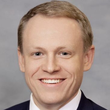 Smiling man in a suit and tie against a gray background.