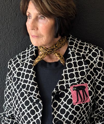 Elderly woman wearing a patterned jacket and leopard print neck scarf.