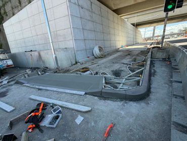 Road construction site under a highway bridge with fresh concrete and tools scattered around.