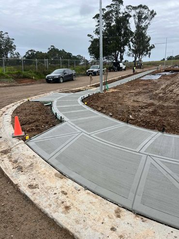Newly poured concrete sidewalk curving along a construction site with vehicles and workers.