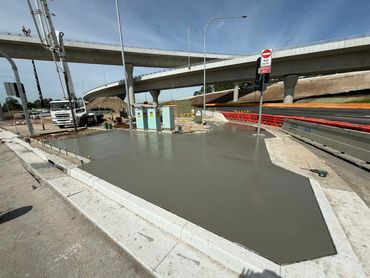 Newly poured concrete slab at a highway construction site under an overpass.