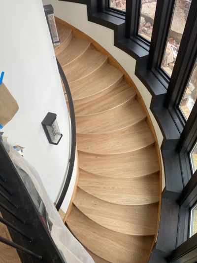 Curved wooden staircase with black window frames and natural light.
