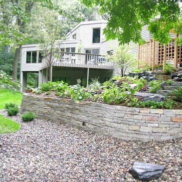 Modern house with terraced garden and stone retaining wall.