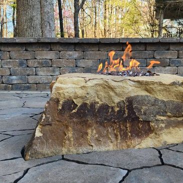 Outdoor fire pit on a large natural stone with a brick wall background.