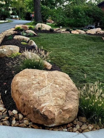 Landscaped garden with large rocks and green lawn under trees.