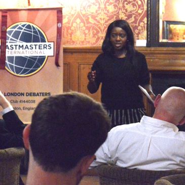 Debate meeting at 104 London Debaters, a debate club in London. A black woman stands before people d