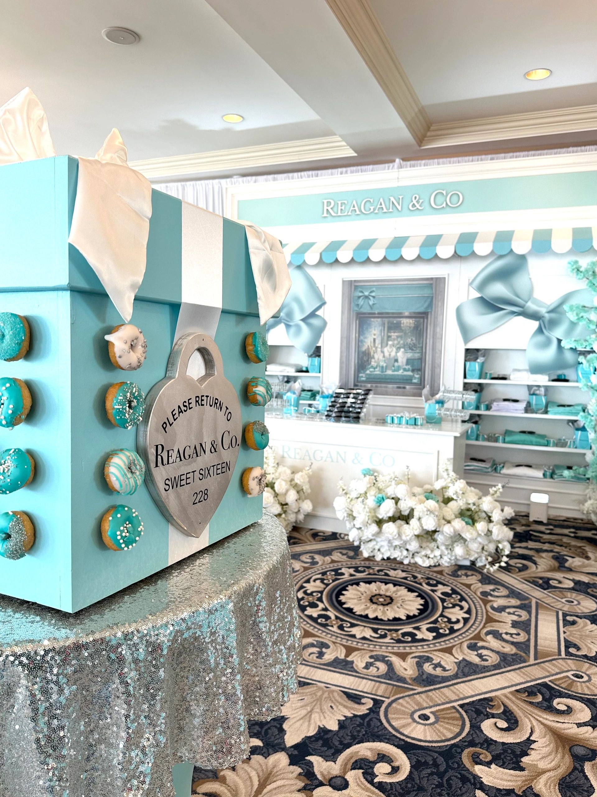 Elegant blue-themed Sweet Sixteen party setup with a giant gift box and floral decorations.