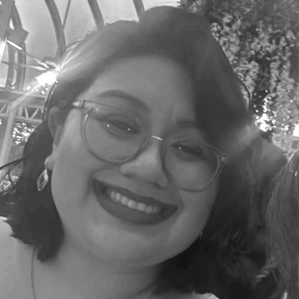 Smiling woman with glasses and earrings in a softly lit setting.
