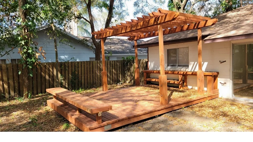 A small wooden porch with a terrace, bar, and bench in a backyard.
