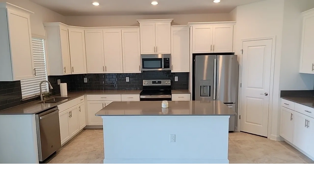 A well lit white kitchen with granite countertops and new stainless steel kitchen appliances.