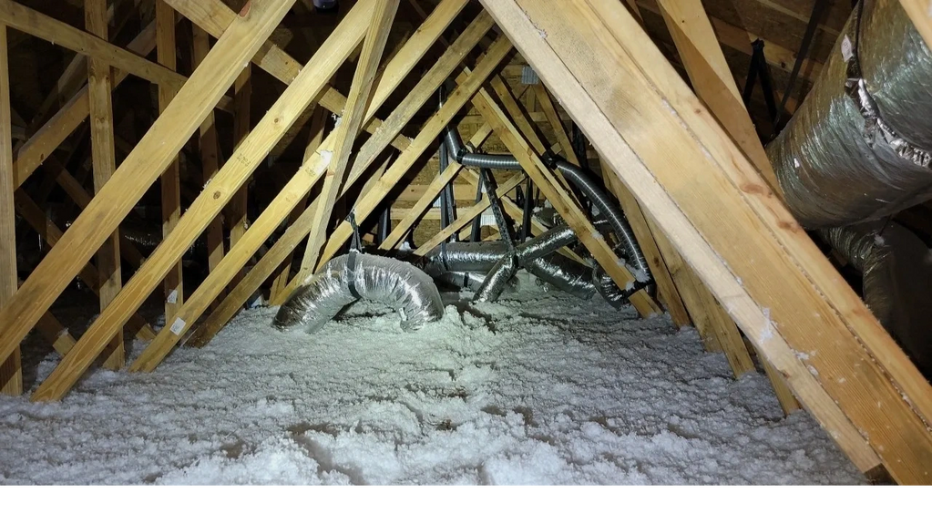 A dusty roof structure and attic showing piping and wood beams.