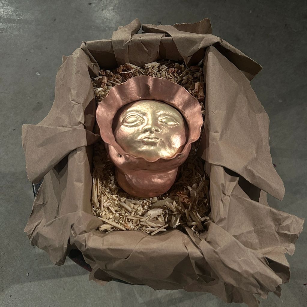 A metallic face sculpture wrapped in brown paper.