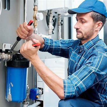 A plumber fixing a water filtration system indoors.