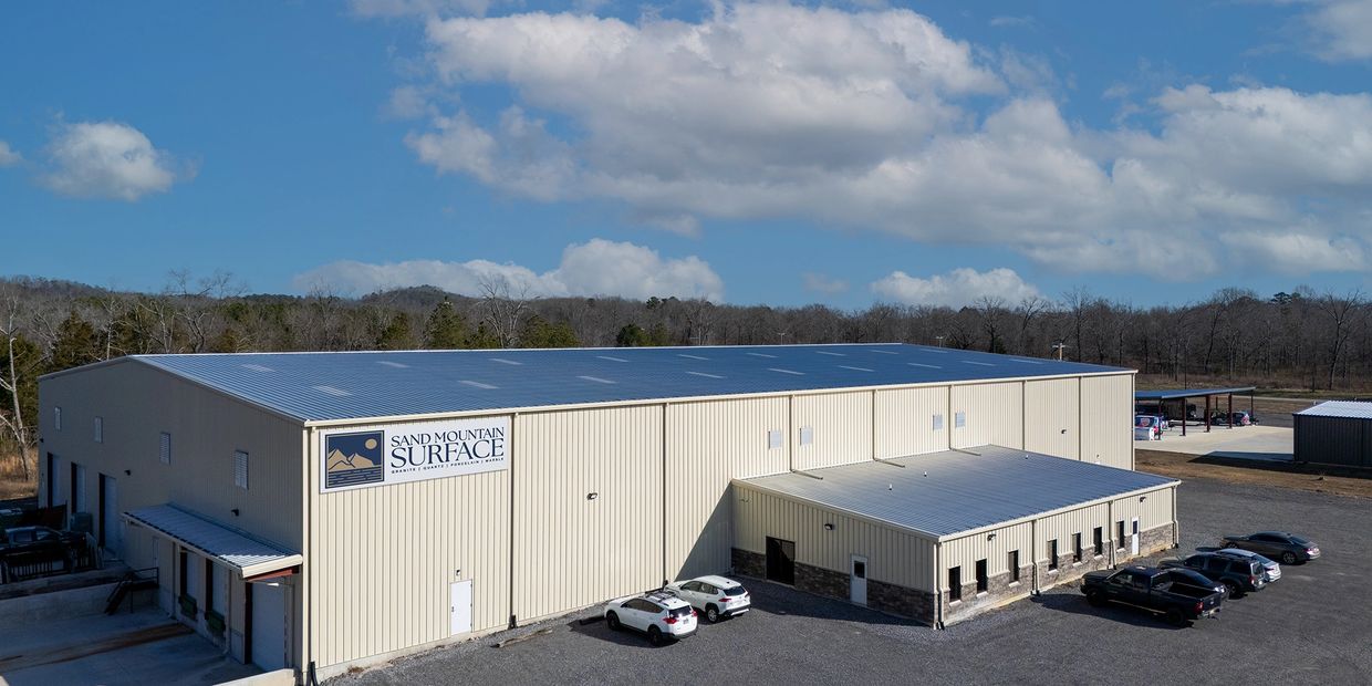 Large industrial building with cars parked outside under blue sky.