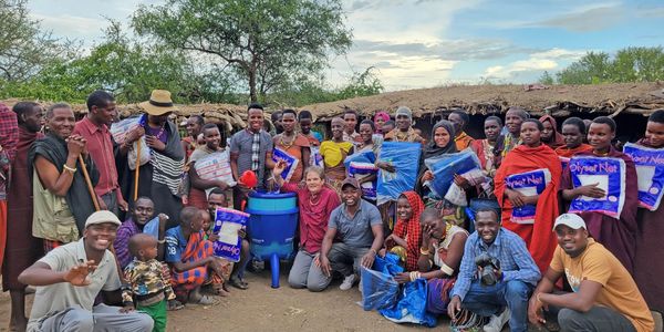 A large group of people smiling and posing outdoors with supplies in a rural setting.