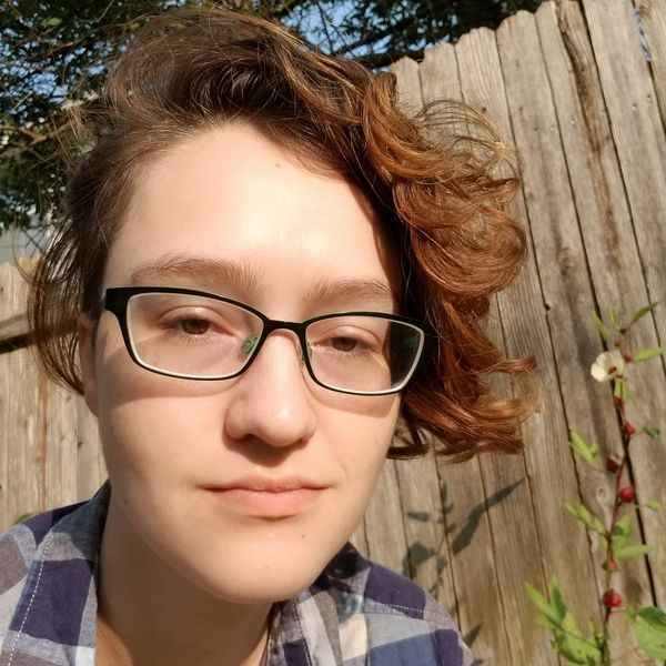Person with glasses and curly hair outdoors in sunlight.