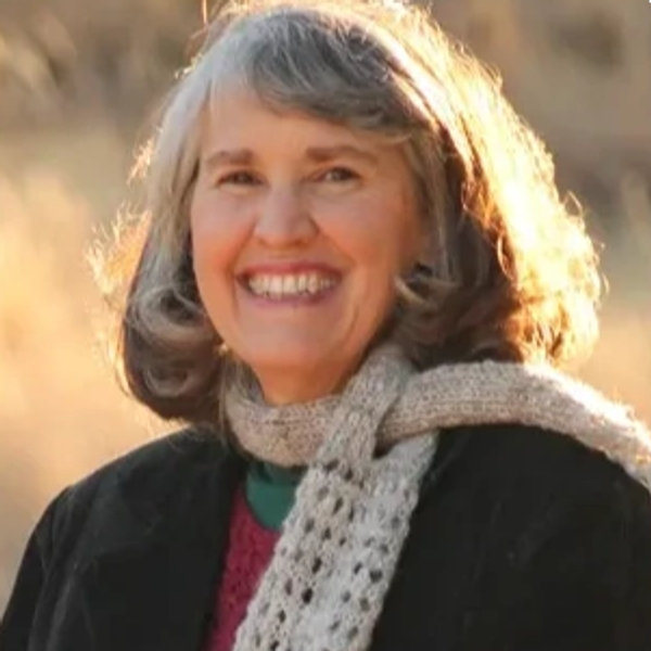 Smiling woman in a warm scarf outdoors with sunlight in background.