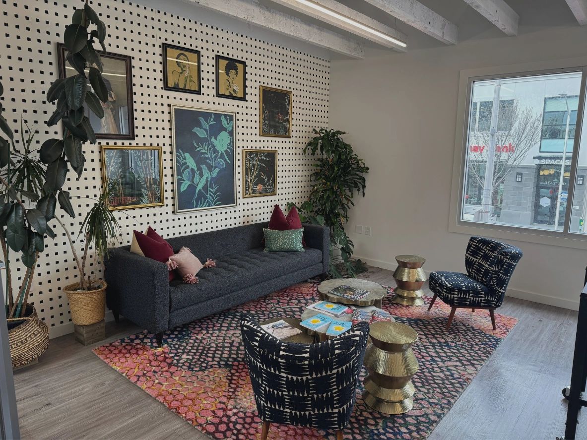 Cozy living room with patterned rug, dark sofa, two chairs, plants, and framed art on dotted accent wall.