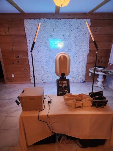 Photo booth setup with floral backdrop and neon sign.