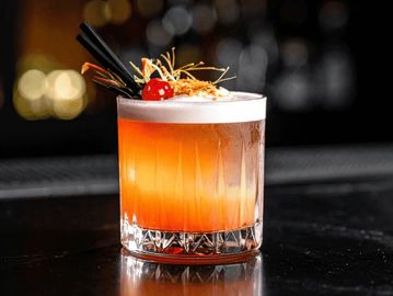 A vibrant orange cocktail with a frothy top and cherry garnish.
