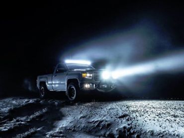 A pickup truck with bright headlights driving at night in a snowy area.